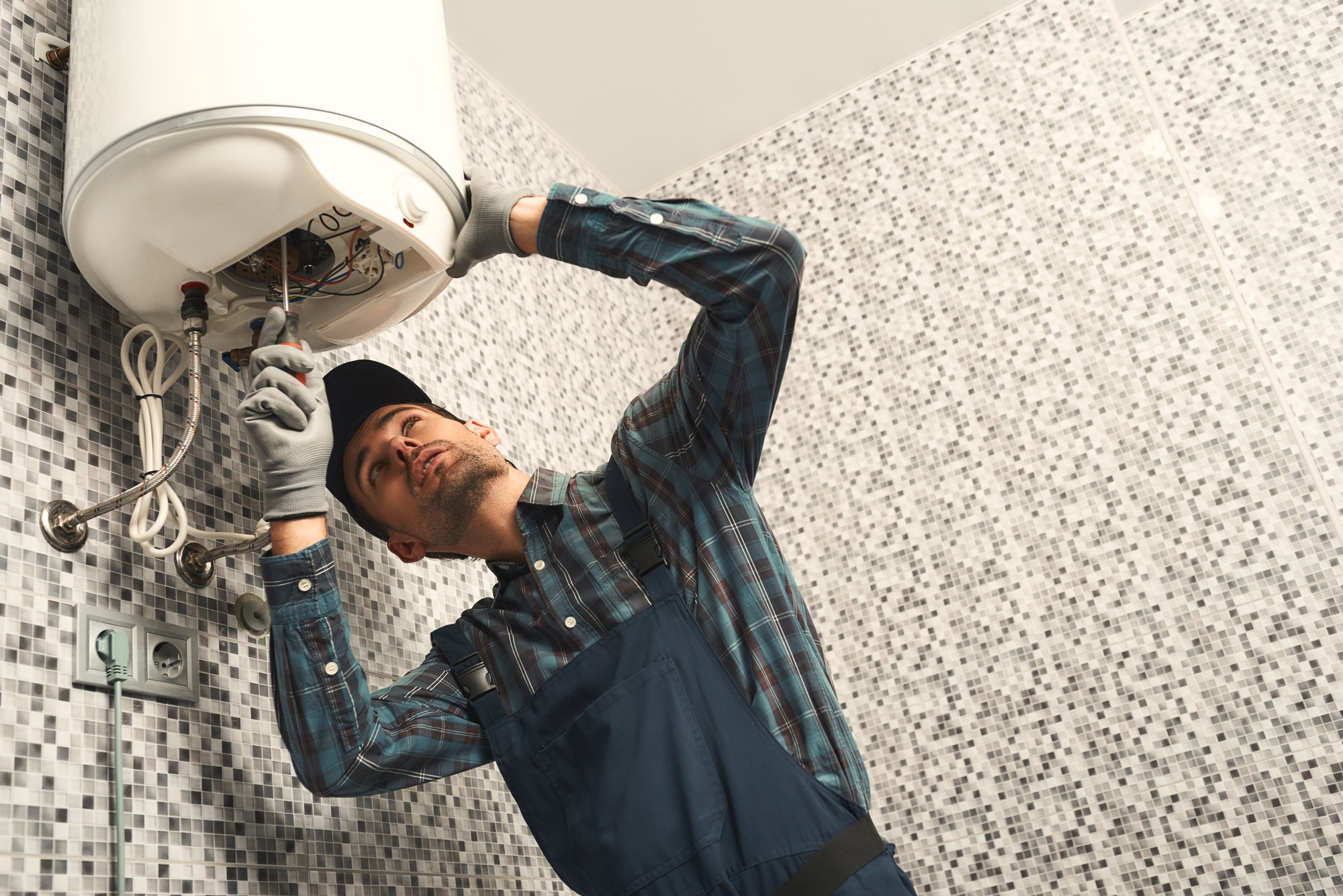 Plumber installing electric heating boiler. Young handyman in uniform setting up electric heating